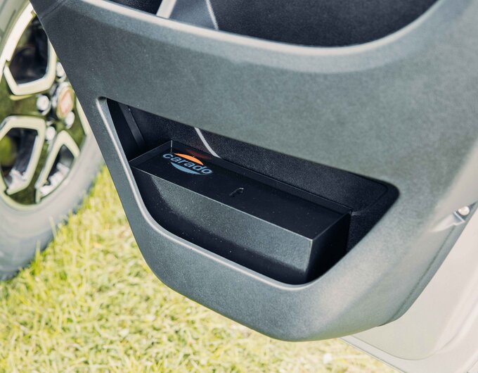 Storage compartment in the open door of a Carado motorhome, detailed view with wheel in the background