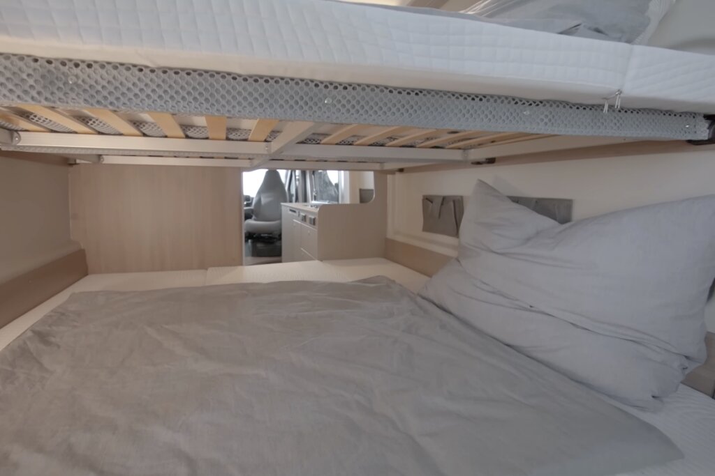 Schlafbereich im Carado Wohnmobil mit Doppelbett, Hubbett darüber und Blick nach vorn in den Innenraum