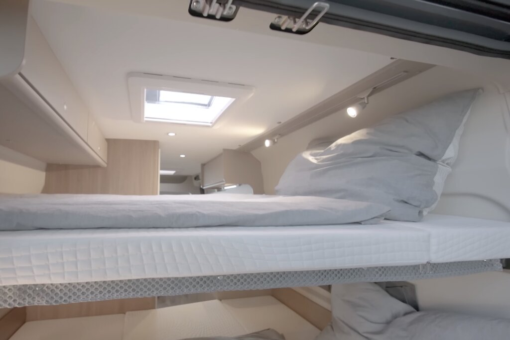 Innenraum Carado Wohnmobil mit Hubbett, Matratze, Kissen und Dachfenster über dem Schlafbereich