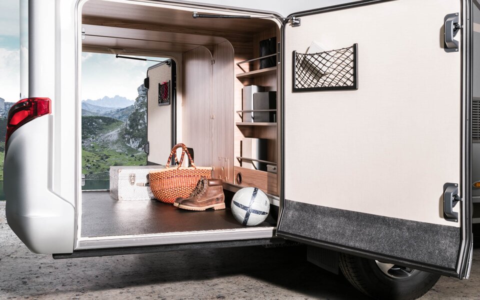 The rear garage of the Hymermobil is open on both sides and loaded with a ball, shoes, shopping basket and suitcase