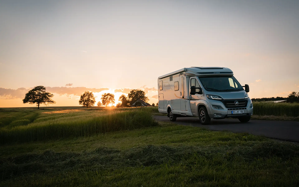 HYMER Exsis-t on a narrow street amid green meadows and cornfields at sunset