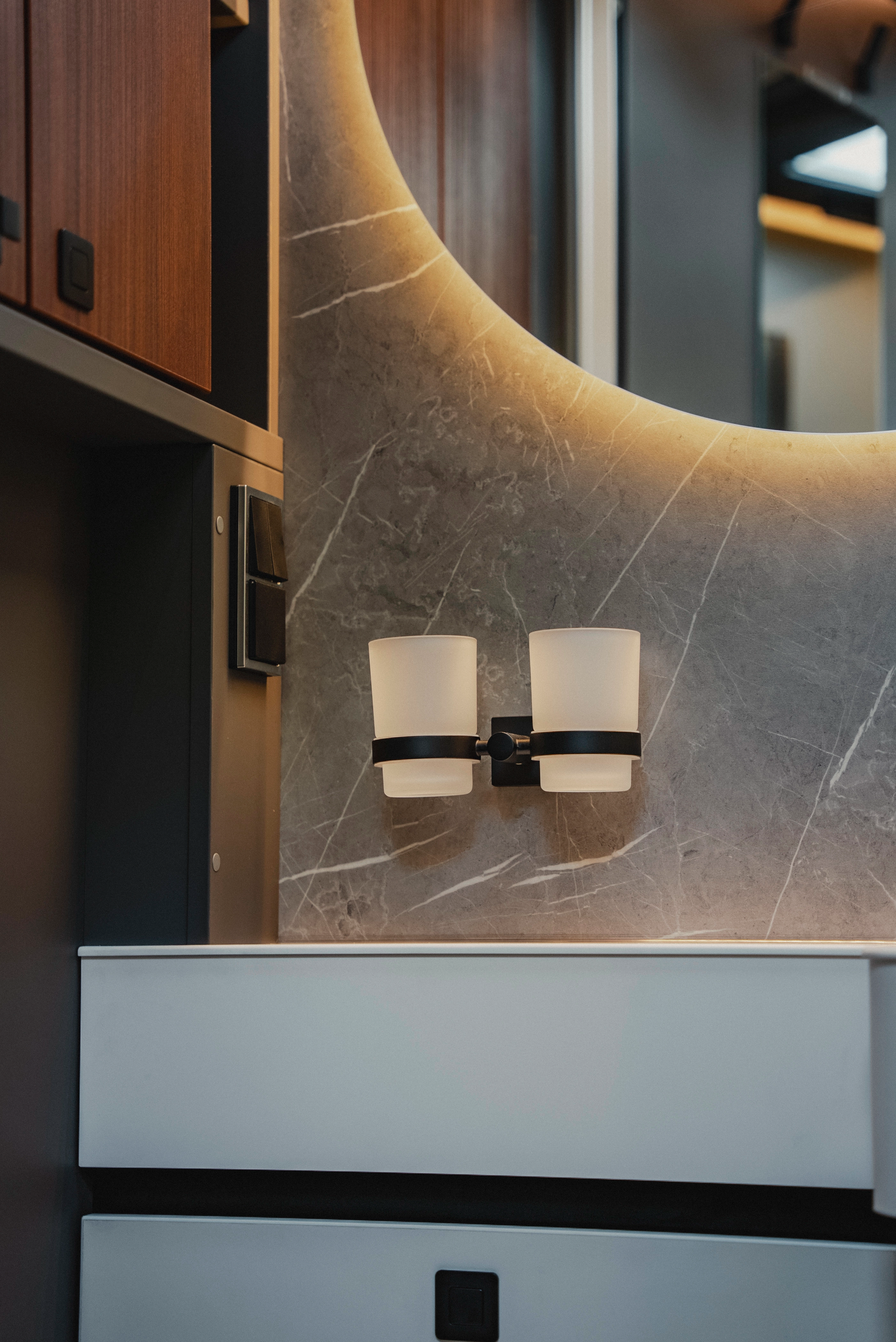 Thoughtful details stylishly implemented: The cup holder blends with the noble surface of the side wall, the modern washbasin, and the backlit, round mirror to form a harmonious overall artwork.